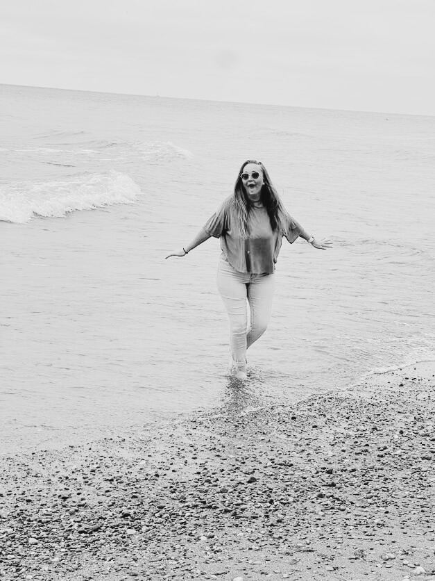 Kristen B. Lenzen laughing with arms wide open at the water's edge